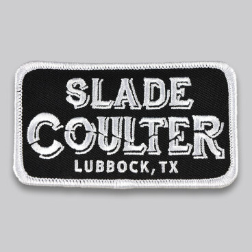 Black patch with white embroidery displaying a name and location.