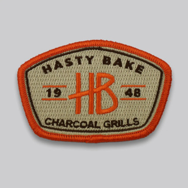 Badge-shaped patch with text "HASTY BAKE HB CHARCOAL GRILLS 1948" in orange and black.