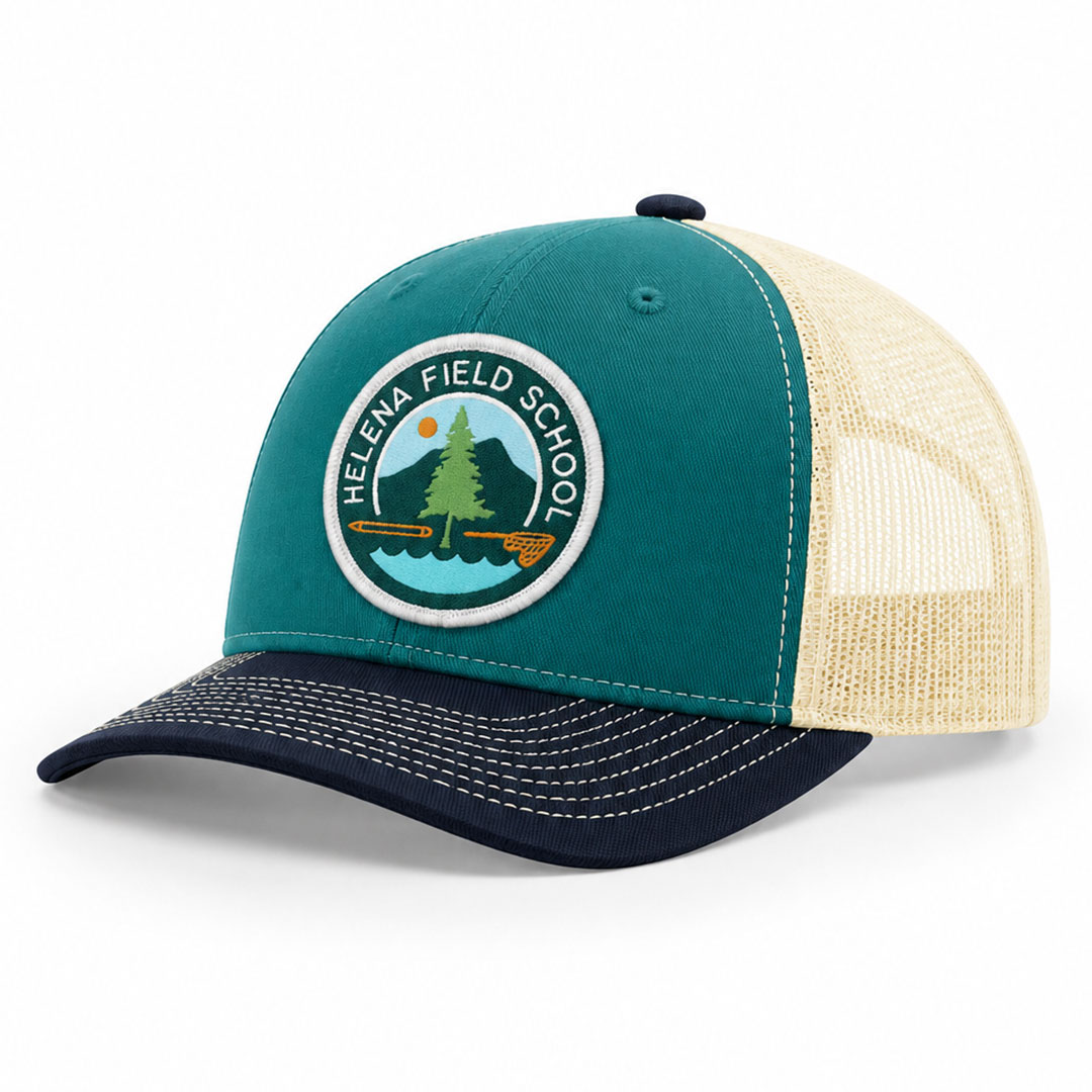 Teal and navy Richardson 112 trucker cap with a round embroidered Helena Field School patch on the front panel.