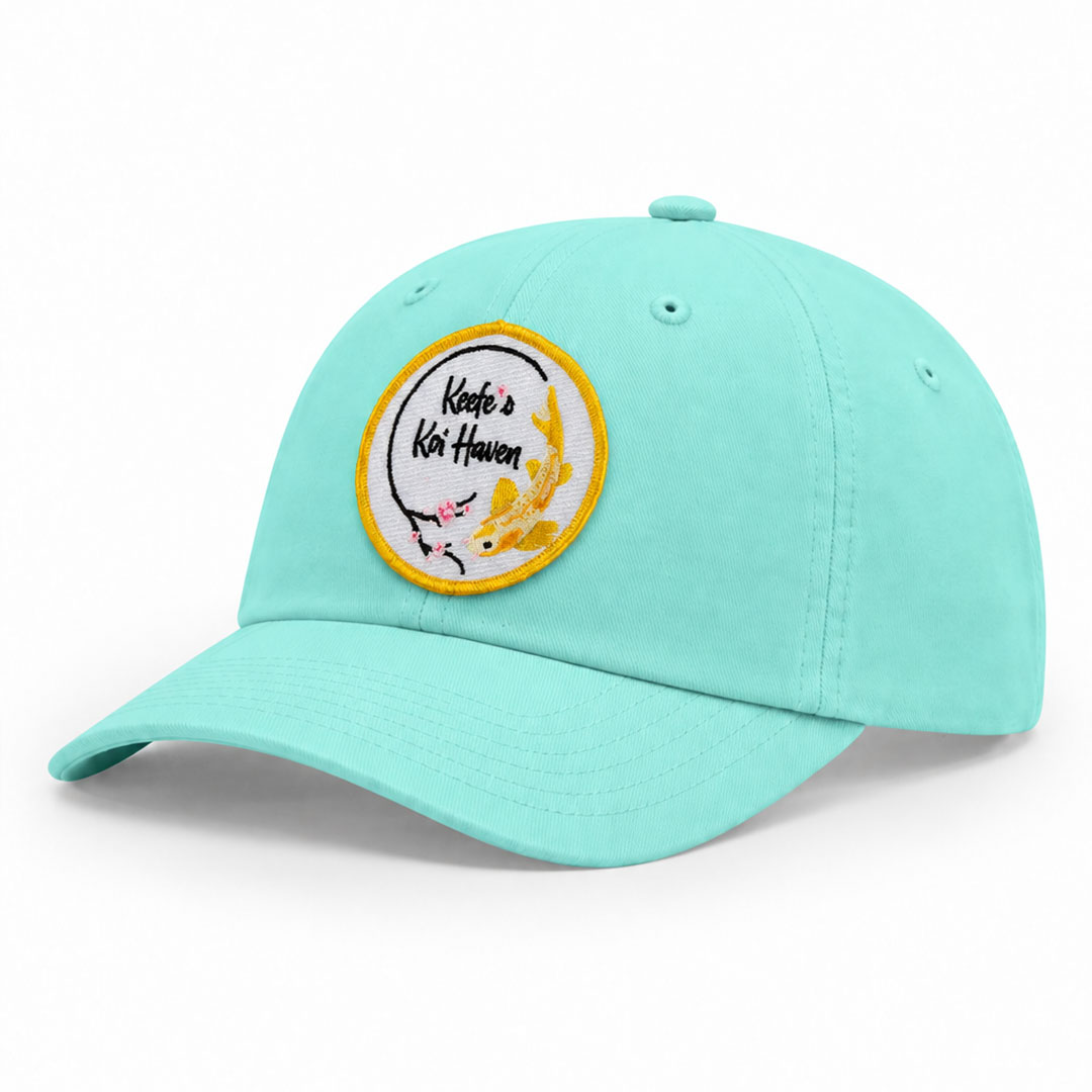 Mint green X210P performance cap with a round embroidered Keefe’s Koi Haven patch on the front.