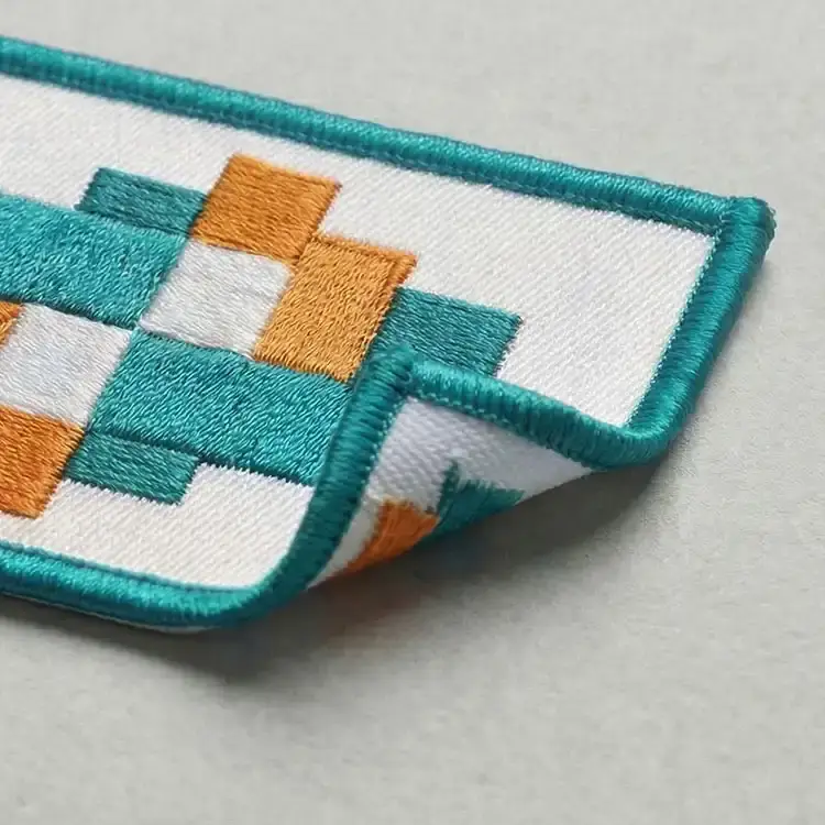 A standard embroidered patch with a teal Merrow border and orange and teal stitching, its corner turned up to show the sew-on back